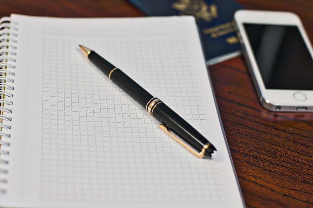 Black pen on a grid notebook with smartphone and passport on