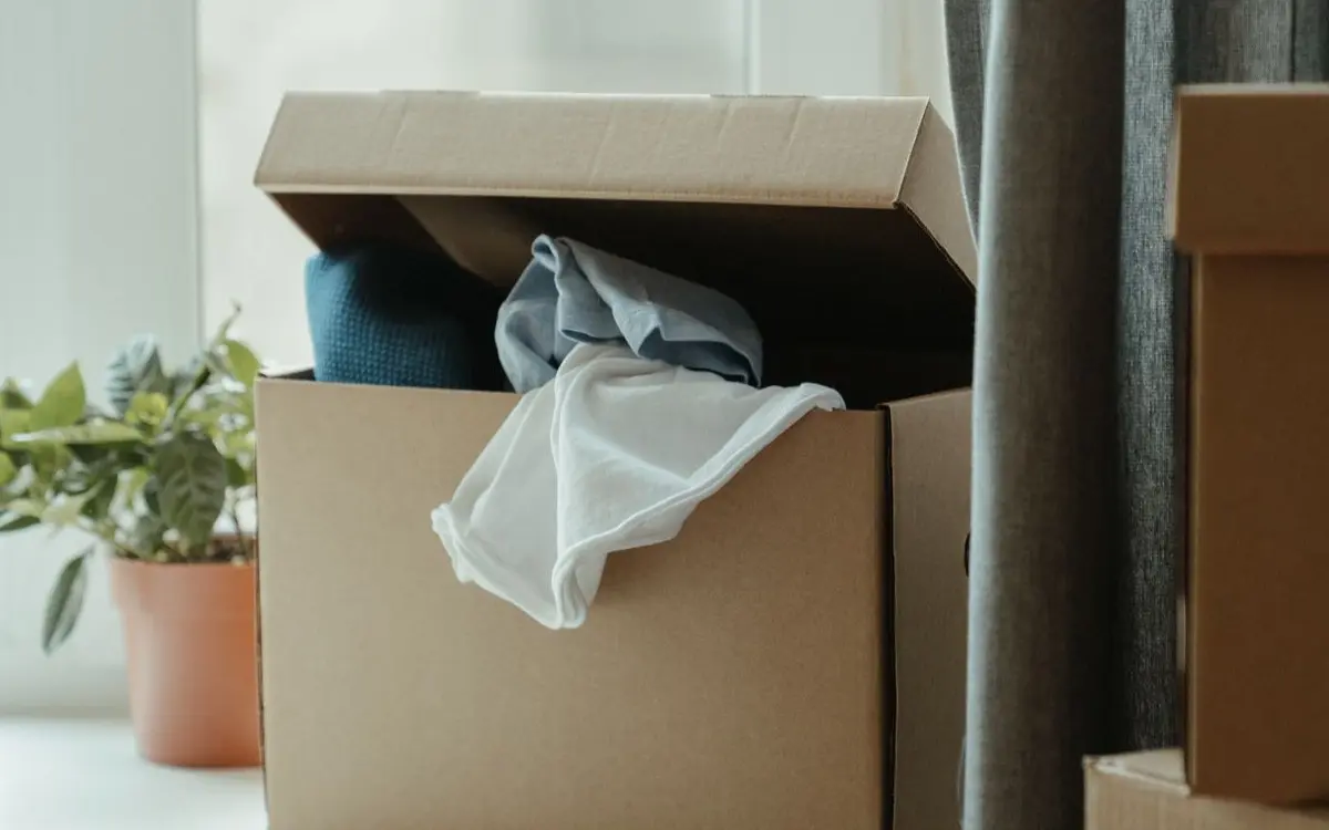 Open cardboard box with clothes by window, symbolizing movin